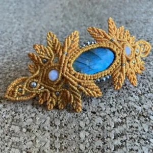 Zoom barrette en micro-macramé orange topaze, cabochon labradorite, perles en pierre de Lune et acier inoxydable, vue de 3/4 posée sur planche de travail en liège