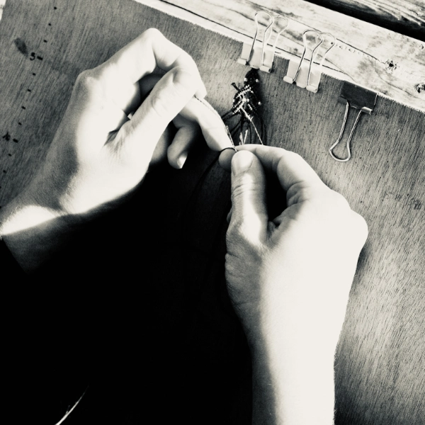 Zoom mains tissant un sapin en micro-macramé