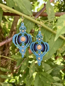 Boucles d'oreille en micro-macramé bleu turquoise, noir et bleu marine, perle centrale jaspe paysage, effet rayonnant, perles en laiton, arrière plan végétation