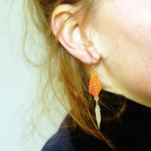 Boucle d'oreille losange en micro-macramé orange topaze, perle en acier inoxydable et plume en métal, zoom porté, cheveux roux