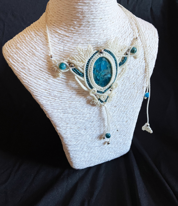 Zoom collier en micro-macramé blanc et émeraude, cabochon en apatite, perles en apatite et acier inoxydable, motifs feuilles, vue 3/4 sur présentoir neutre