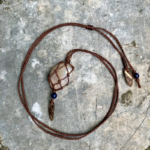 Pendentif en micro-macramé marron acajou, galet naturel serti en filet, perles en lapis lazuli et morceaux de coque de noix de coco, posé sur une pierre plate