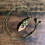 Pendentif en micro-macramé vert olive, élément en bois massif : merisier, perles en jaspe paysage, posé sur une table en bois