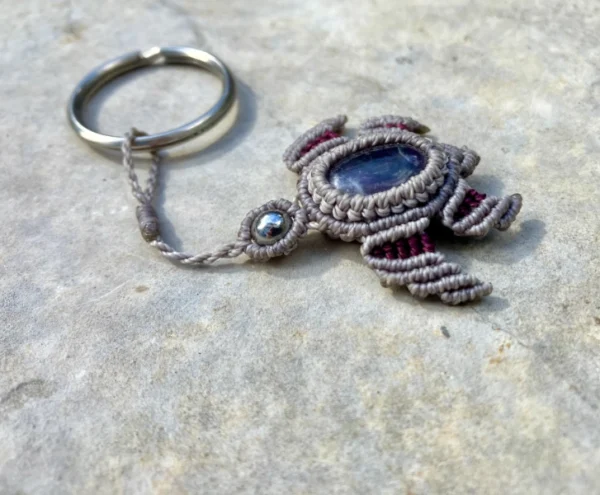Porte-clefs en micro-macramé 3D, vue de 3/4, tortue marine gris et prune, carapace : cabochon améthyste, tête : perle en acier inoxydable, anneau en acier inoxydable