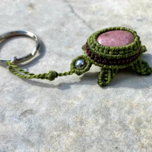 Porte-clefs en micro-macramé 3D, vue de 3/4, tortue terrestre vert olive et prune, carapace : cabochon rhodonite, tête : perle en acier inoxydable, anneau en acier inoxydable