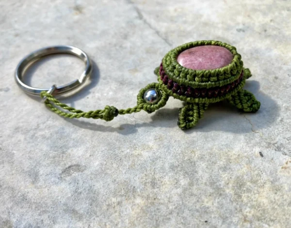 Porte-clefs en micro-macramé 3D, vue de 3/4, tortue terrestre vert olive et prune, carapace : cabochon rhodonite, tête : perle en acier inoxydable, anneau en acier inoxydable