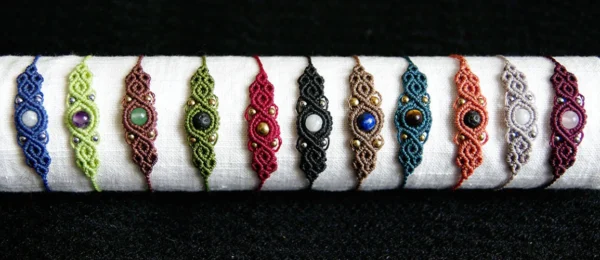 11 bracelets en micro-macramé bleu marine, vert citron, acajou, vert olive, bourgogne, noir, cèdre, sarcelle cannelle, gris prune, motifs arabesques, support blanc fond noir
