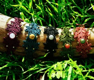 5 Bracelets en micro-macramé différentes couleurs, motifs feuilles et entrelacs, sur un support en bois, arrière plan végétation