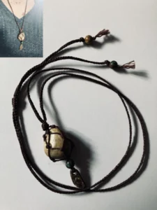 Collier en micro-macramé marron café, galet naturel serti en filet, perles turquoise d'Afrique et morceau de noix de coco, vue posé sur une table et miniature porté