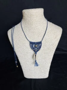 Collier en micro-macramé bleu marine, coquillage cauri et perles laiton, vue de face sur présentoir neutre, fond noir