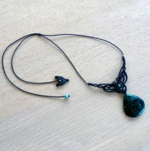 Collier sobre en micro-macramé noir et émeraude, pierre gemme et perles en émeraude, perles en acier inoxydable, posé sur une table en bois
