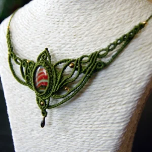 Collier asymétrique en micro-macramé vert olive, cabochon en verre rayé orange blanc et vert, perles en laiton, breloque goutte en laiton émaillé noir, vue 3/4 sur un présentoir neutre