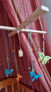 Zoom mobile coloré accroché au-dessus d'un berceau, papillons en micro-macramé et perles en bois, pierre de Lune