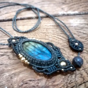 Zoom vue 3/4 pendentif en micro-macramé gris anthracite, cabochon et perle en labradorite, perles en laiton, motifs simples, sur table en bois