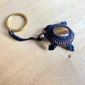 Porte-clefs Tortue terrestre en micro-macramé noir et acajou, vue 3/4, tête : perle en laiton, carapace : cabochon en œil de tigre, anneau en acier inoxydable doré