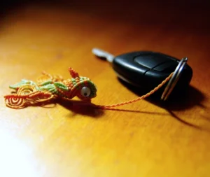 Porte-clefs petite carpe koï orange topaze et vert citron, yeux mobiles, anneau en acier inoxydable, attaché à une clef de voiture, vue 3/4, support table bois