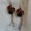 Boucles d'oreilles Trio floral suspendue sur un tissu beige. Fils orange cannelle, cuivre et acajou, perles en laiton et attaches en acier inoxydable doré à l'or fin