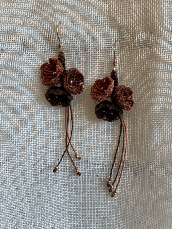 Boucles d'oreilles Trio floral suspendue sur un tissu beige. Fils orange cannelle, cuivre et acajou, perles en laiton et attaches en acier inoxydable doré à l'or fin