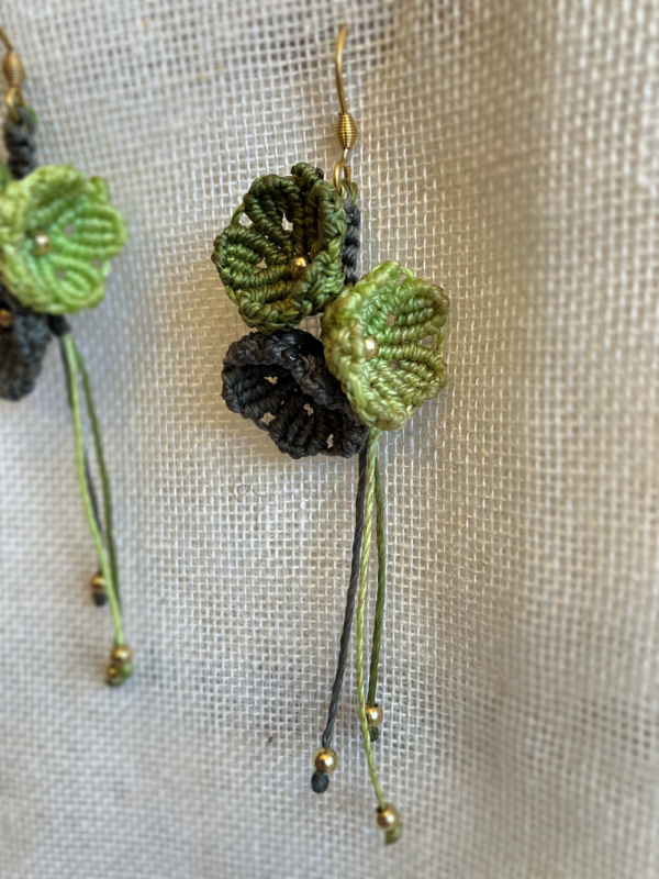 Zoom sur une boucle d'oreille Trio floral suspendue sur un tissu beige. Fils vert olive, khaki et citron, perles en laiton et attaches en acier inoxydable doré à l'or fin