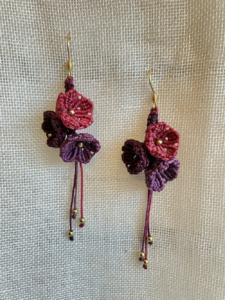 Boucles d'oreilles Trio floral suspendue sur un tissu beige. Fils prune, améthyste et rose framboise, perles en laiton et attaches en acier inoxydable doré à l'or fin