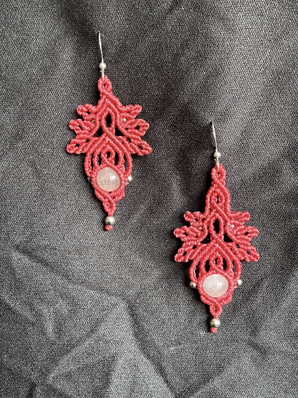 Photo boucles d'oreilles aux motifs feuilles et entrelacs en micro-macramé rose framboise, perles en quartz rose, perles et crochets en acier inoxydable, accrochées sur un tissu noir