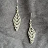Photo boucles d'oreilles en forme de feuille en micro-macramé vert khaki, perles et crochets en acier inoxydable, accrochées sur un tissu noir