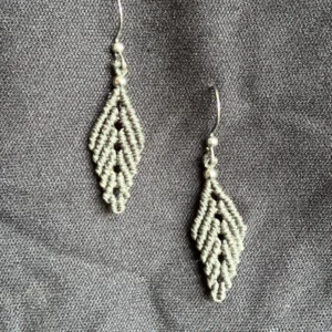 Photo boucles d'oreilles en forme de feuille en micro-macram&eacute; vert khaki, perles et crochets en acier inoxydable, accroch&eacute;es sur un tissu noir