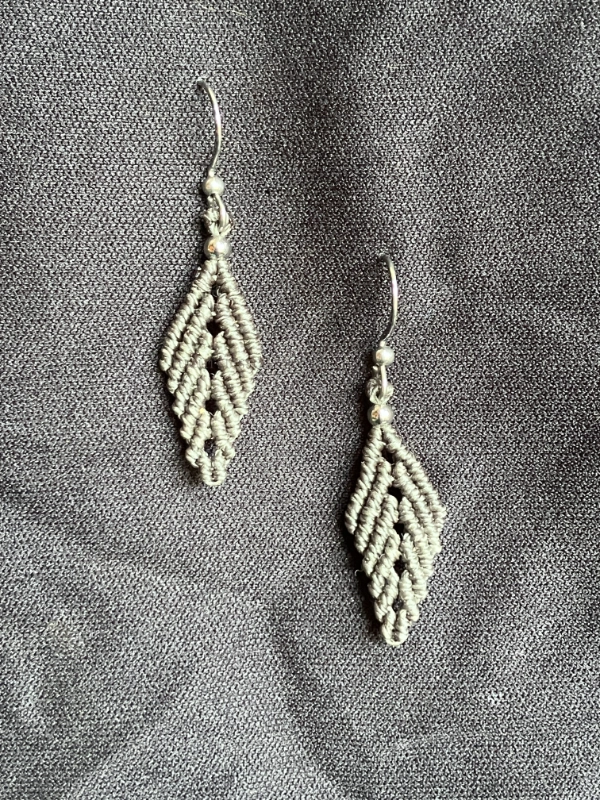 Photo boucles d'oreilles en forme de feuille en micro-macramé vert khaki, perles et crochets en acier inoxydable, accrochées sur un tissu noir