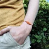 Photo détail d'un bracelet au motif feuille en micro-macramé jaune topaze et perles en acier inoxydable, porté, main dans la poche, végétation en arrière-plan