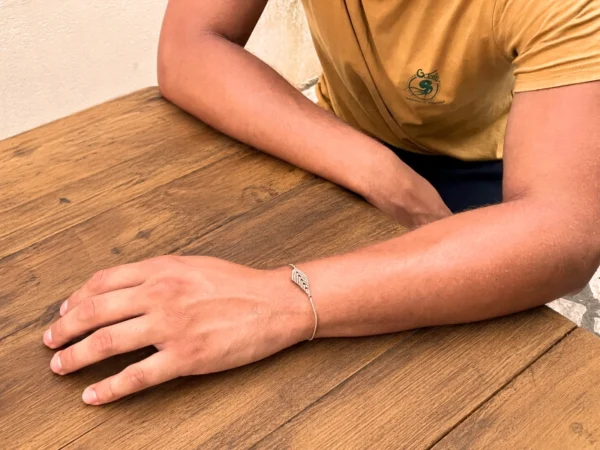 Photo bracelet à motif feuille en micro-macramé beige, porté par un homme, arrière plan table en bois