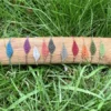 Photo 10 bracelets en micro-macramé de différentes couleurs, motif feuille simple, exposés sur un support en bois clair, herbe en arrière-plan