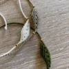 Photo de trois bracelets à motif feuille en micro-macramé blanc naturel, beige et vert olive, posés sur une table en bois clair