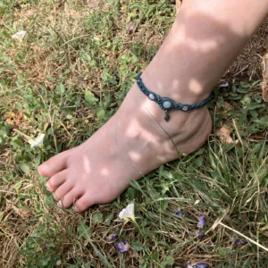 Photo bracelet de cheville en micro-macramé émeraude avec perles en amazonite et pierre de Lune, perles et breloque losange en acier inoxydable, porté, arrière plan herbe