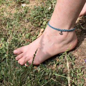 Photo bracelet de cheville en micro-macramé bleu turquoise avec breloque en forme d'ancre marine en acier inoxydable, porté, arrière plan herbe