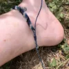 Photo bracelet de cheville en micro-macramé bleu marine, turquoise, blanc et noir porté, zoom sur le nœud coulissant, arrière plan herbe