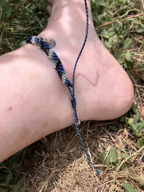 Photo bracelet de cheville en micro-macramé bleu marine, turquoise, blanc et noir porté, zoom sur le nœud coulissant, arrière plan herbe